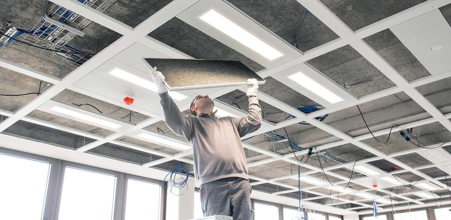 A man installing sound-absorbing panels to an office ceiling