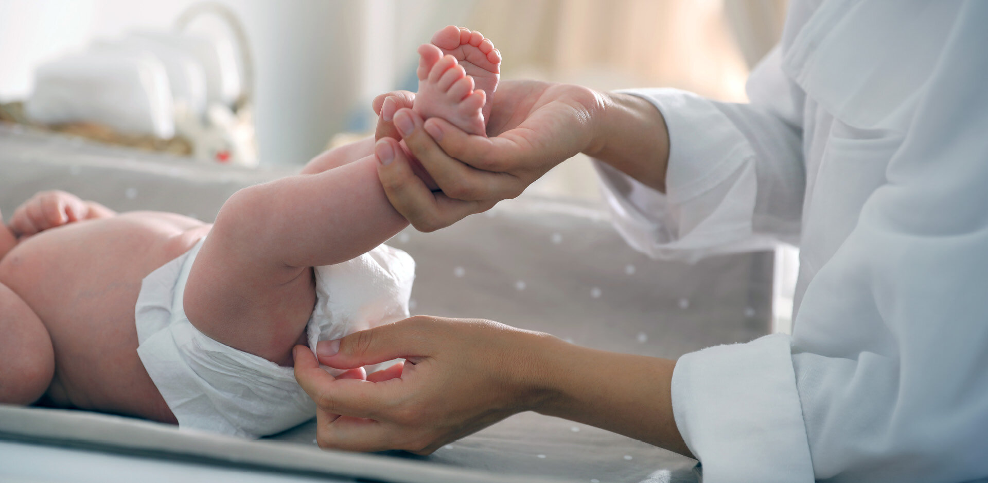 Jemand prüft die Windel eines Babys, das auf einem Wickeltisch liegt.