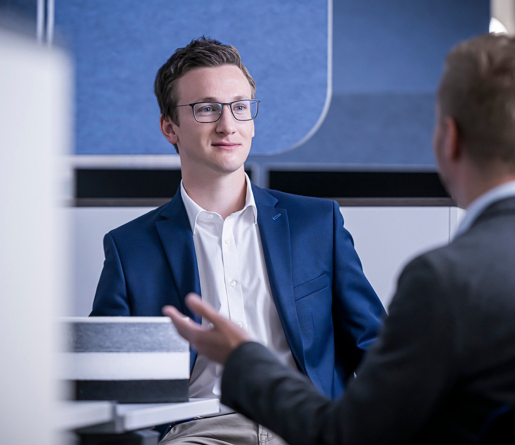 A young man in a suit talks to another man.