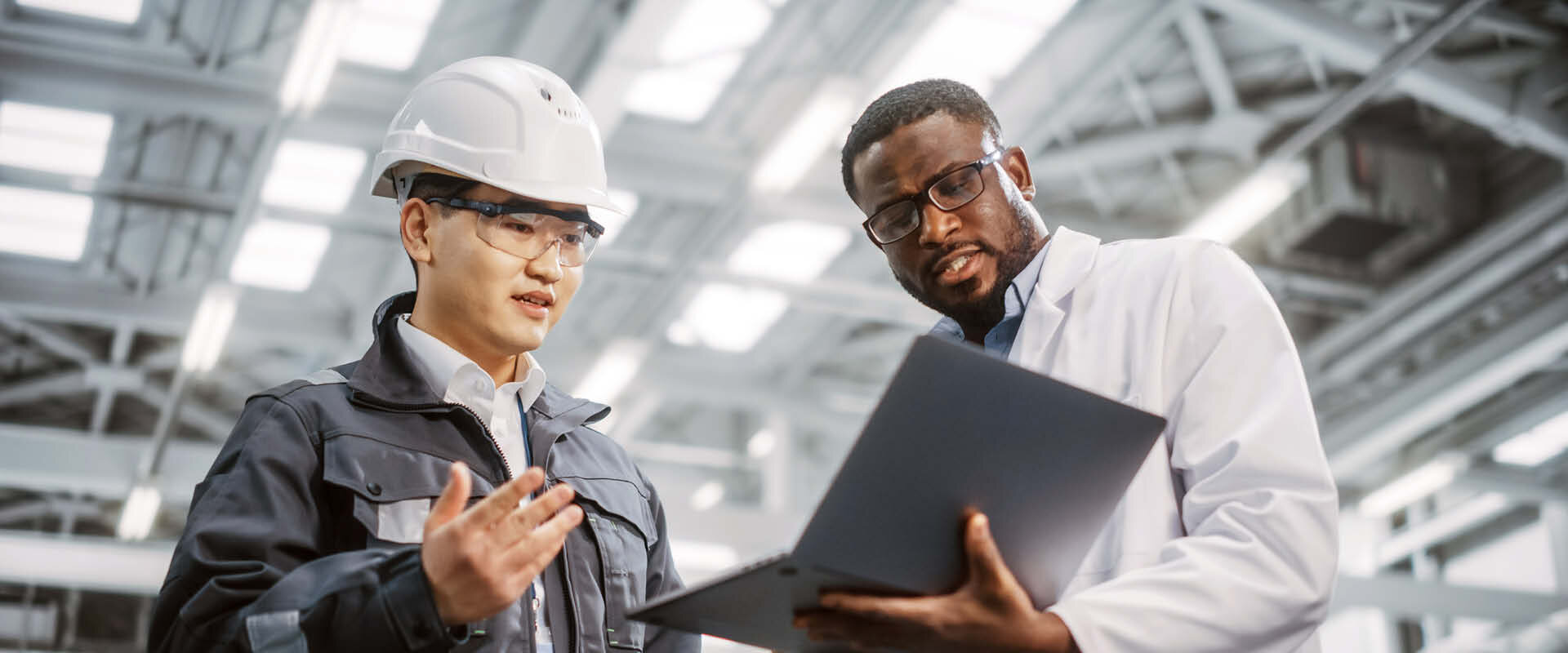  Zwei Männer bei Besprechung am Laptop in einer Werkshalle | Sandler Group